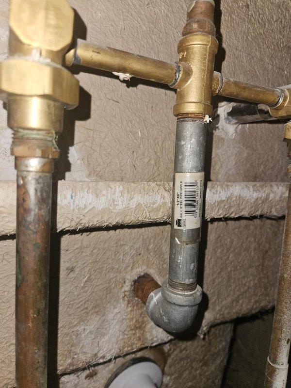 Responded to reported leak at bathroom tub shower drain with easy access. Inspected underfloor plumbing assembly consisting of white PVC drainage pipes and fittings installed between floor joists, noting signs of age and weathering on surrounding wooden structural elements. Evaluated brass supply piping, valves, and galvanized steel connections mounted to concrete block wall in utility area. Documented existing plumbing configuration and leak location with photographic evidence for service records.