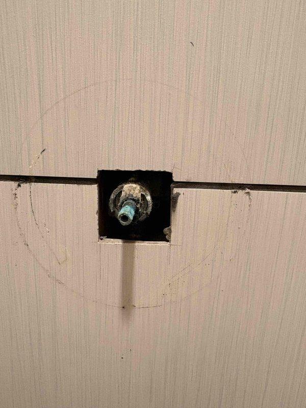 Responded to reported leak at shower handle fixture. Upon arrival, accessed plumbing connections through wall cavity to identify source of water intrusion. Inspected shower valve assembly and supply line connections, identifying compromised valve body with turquoise-colored base and threaded connection requiring attention. Created access opening in wall to properly reach and service the affected plumbing components, exposing brass shutoff valve and supply fittings for repair work.
