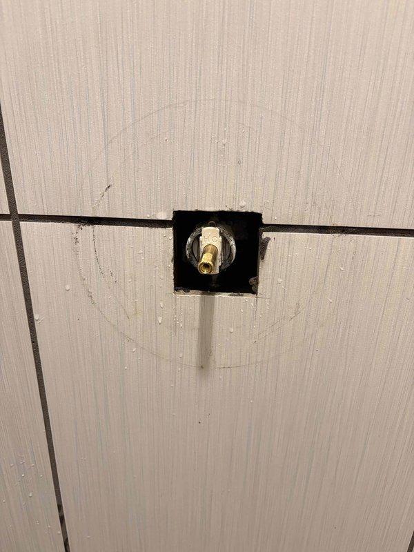 Responded to reported leak at shower handle fixture. Upon arrival, accessed plumbing connections through wall cavity to identify source of water intrusion. Inspected shower valve assembly and supply line connections, identifying compromised valve body with turquoise-colored base and threaded connection requiring attention. Created access opening in wall to properly reach and service the affected plumbing components, exposing brass shutoff valve and supply fittings for repair work.