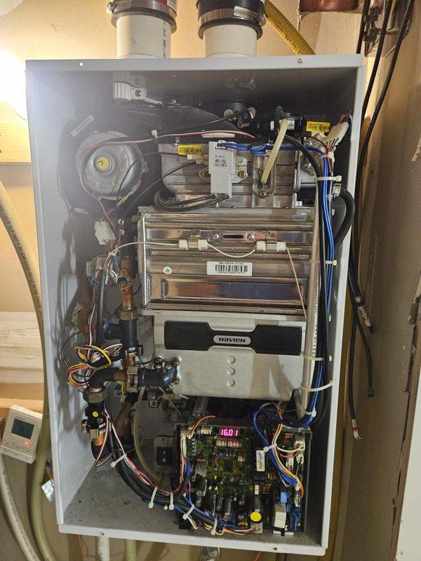 Responded to service call for non-operational water heater at residential property. Upon arrival, accessed basement utility area and inspected wall-mounted Navien tankless water heating unit. Removed front access panel to evaluate internal components including heat exchanger, blower assembly, control board, and gas valve connections. Observed digital display showing error code 180.1, indicating potential issue with internal sensor or operational parameter. Verified all PVC exhaust and intake venting connections secure at top of unit. Inspected control board, wiring harnesses, and electrical connections for signs of failure or loose connections. Evaluated heat exchanger condition, copper and plastic tubing connections, and gas valve assemblies for proper operation. Assessed blower motor and fan assembly functionality. Documented unit condition with photographic evidence showing internal components and installation environment. Provided diagnostic findings and recommended repair options 