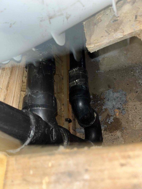 Responded to plumbing fixture issue requiring access to under-floor drainage system. Created access openings in interior wall to expose concealed plumbing infrastructure, revealing black ABS/PVC drainage pipes with fittings running horizontally through floor joists. Assessed condition of existing drainage components and structural framing in confined crawl space area. Completed necessary fixture repair/replacement work with access through wall cavity and subfloor area.