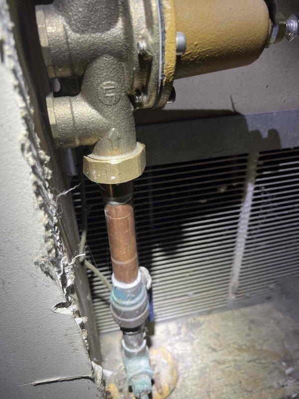 Responded to rental property for complaint of very low water pressure throughout the residence. Investigated mechanical closet and located 20+ year old pressure regulator valve exhibiting signs of internal failure and sticking operation. Confirmed inadequate downstream pressure readings consistent with failed pressure reducing valve. Documented existing brass valve assembly and copper piping configuration with photographic evidence showing corrosion on copper lines and aged valve components.