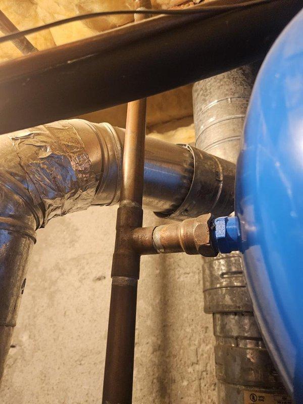 Responded to service call for leaking water heater in residential property. Upon arrival, conducted thorough inspection of standard tank-type water heater system, which was reported to be over 10 years old. Investigation revealed active water leakage from the water heater unit requiring immediate attention.

Performed comprehensive assessment of plumbing infrastructure in utility area, including examination of copper supply lines, shut-off valves, and connection points. Inspected condition of existing piping system, noting evidence of previous repairs including tape-wrapped sections on copper lines. Evaluated brass valve assemblies and PVC drainage components in the vicinity of the water heater installation.

Documented existing conditions through photographic evidence showing confined workspace environment with aged plumbing components, worn flexible hoses, and signs of moisture accumulation on surrounding surfaces. Assessment included review of wooden structural elements and concrete