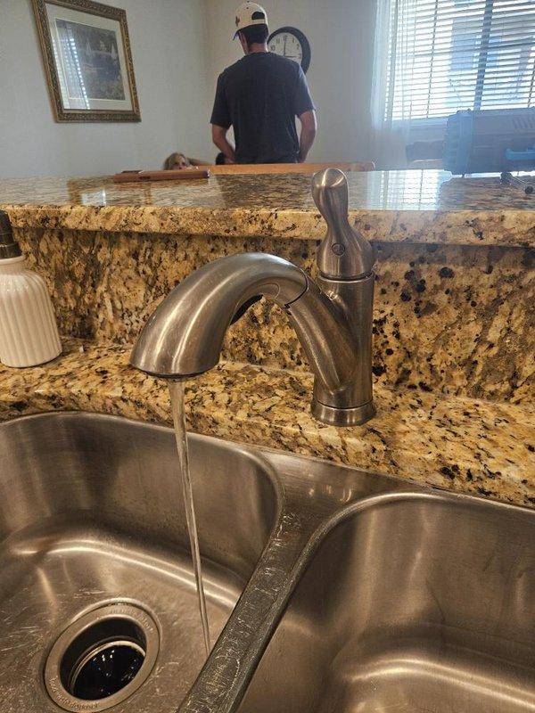 Responded to kitchen faucet leak with steady water flow reported over previous two weeks. Upon arrival, inspected double-basin stainless steel sink with single-handle brushed nickel faucet mounted on granite countertop. Identified loose faucet connections causing water leakage at base. Tightened mounting hardware and supply line connections beneath sink to eliminate leak and restore proper fixture operation.