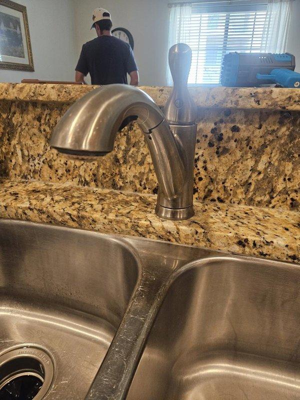 Responded to kitchen faucet leak with steady water flow reported over previous two weeks. Upon arrival, inspected double-basin stainless steel sink with single-handle brushed nickel faucet mounted on granite countertop. Identified loose faucet connections causing water leakage at base. Tightened mounting hardware and supply line connections beneath sink to eliminate leak and restore proper fixture operation.