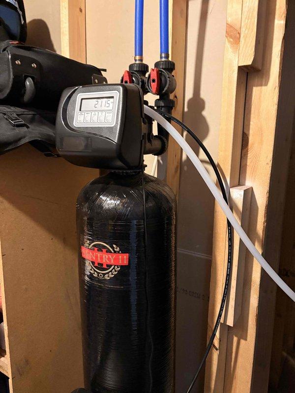 Responded to water quality complaint regarding yellowish-brown discoloration from faucets. Performed diagnostic inspection of 4-year-old water softener system installed in basement, examining control head unit displaying cleaning cycle status, plumbing connections, and overall system operation. Documented system condition including copper and PEX supply lines, brass fittings, control valve assembly, and resin tank to determine cause of water discoloration issue.