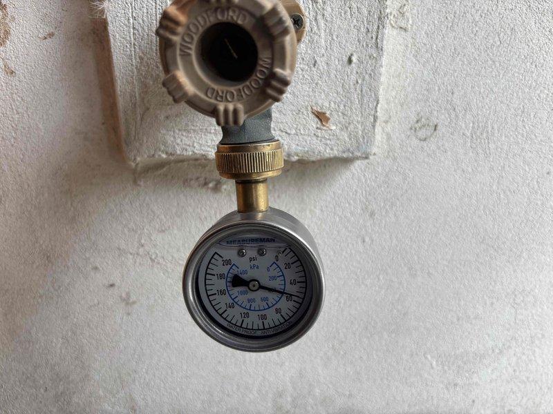 Completed comprehensive plumbing membership inspection including evaluation of 16-year-old tanked water heater located in garage. Inspected water heater compartment, noting standing water accumulation in access area with visible PVC piping and brass fittings. Tested and documented static water pressure at hose bib using calibrated pressure gauge, verifying system pressure levels within operational parameters.