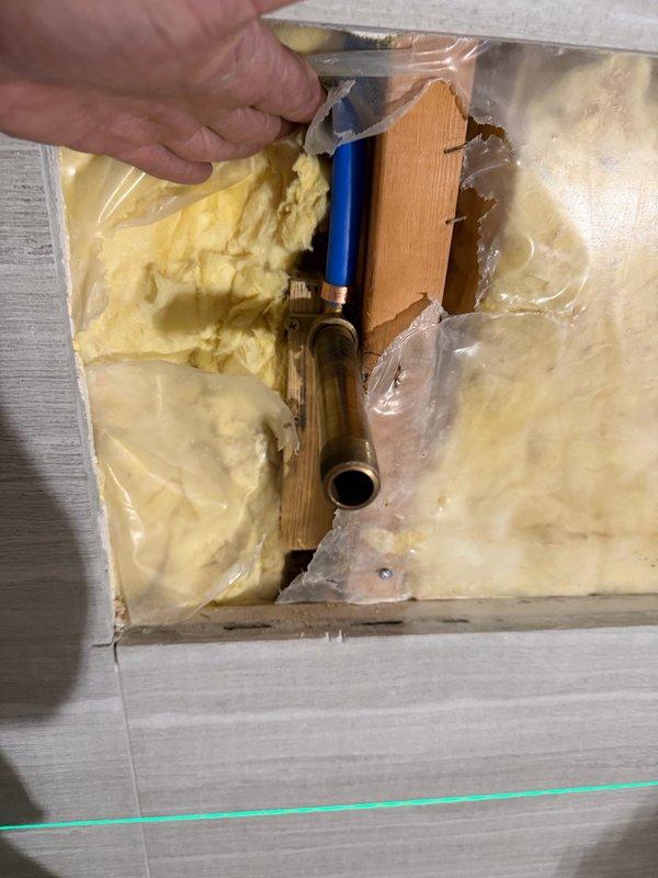 Responded to warranty recall for shower fixture installation and tub hot water issue. Accessed plumbing cavity through wall opening to locate and address mixing valve assembly with copper piping. Reset tub fixture connections and verified proper hot water delivery to resolve temperature control problem.
