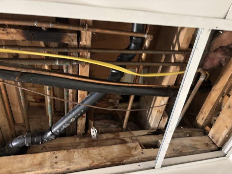 Responded to emergency water leak above shower at residential group home facility. Upon arrival, accessed leak location through ceiling panels as water supply had been shut off to affected area. Inspected exposed plumbing infrastructure including copper supply lines, drainage piping, and associated fittings within ceiling cavity above bathroom fixture. Evaluated system pressure using gauge equipment and assessed condition of existing plumbing installation, noting aged copper piping with surface oxidation and corrugated drainage lines running through wooden joist framing. Identified source of active leak and provided upfront pricing options for repair before proceeding with remediation work.
