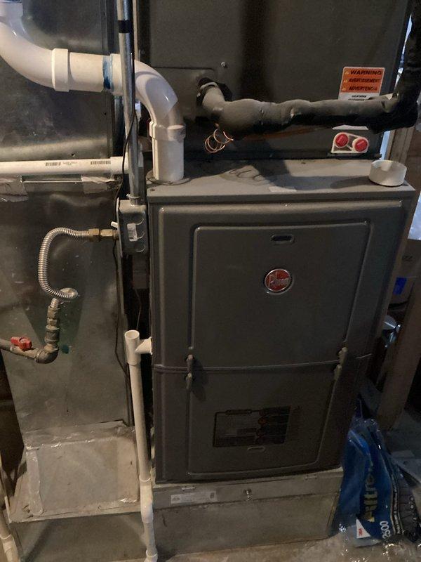 Responded to no cooling complaint on 6-7 year old residential air conditioning system. Performed diagnostic evaluation of Ruud furnace/air handler unit located in basement and outdoor condensing unit on side of property. Inspected electrical connections, control board, and gas line connections on indoor unit. Documented equipment specifications and current operating conditions through visual inspection and photography of nameplate data showing 96,000 BTU/HR input rating and 115V electrical requirements. Completed system assessment to determine cause of AC failure to start.