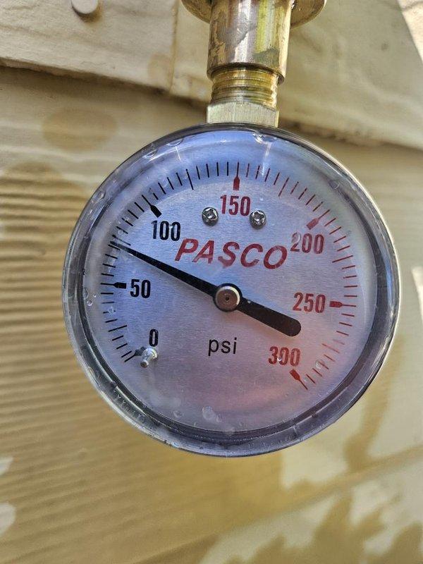Completed kitchen faucet installation and inspected water heater plumbing connections. Verified pressure gauge reading at approximately 75 psi and confirmed proper operation of brass T-valve assembly with flexible supply lines. All connections secured and system tested for leaks.