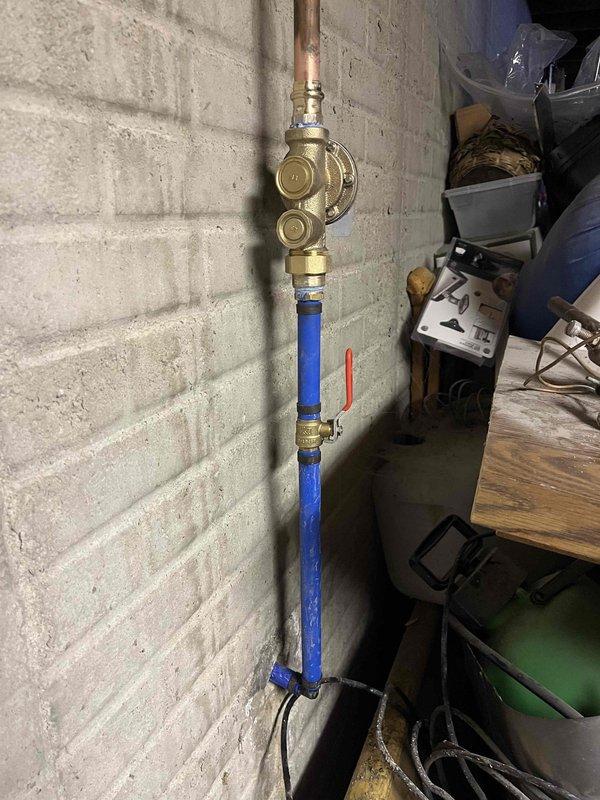 Completed spot repair on main water line penetrating foundation. Installed new pressure reducing valve (PRV) with gauge and new main water shutoff valve with lever handle. Repair was performed at exterior foundation access point where contractor provided excavation. Work included copper pipe connection to brass PRV, followed by blue shutoff valve assembly with brass fittings, all mounted to interior foundation wall.