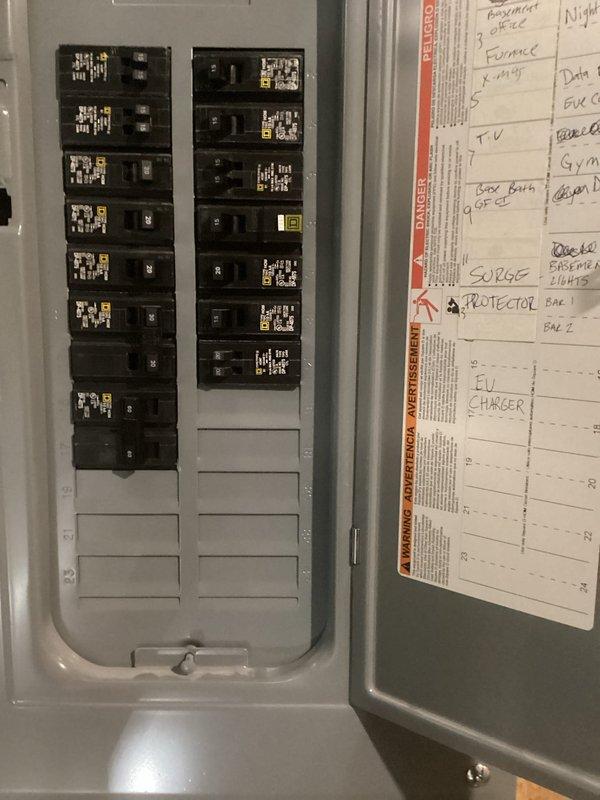 Conducted on-site evaluation for electric vehicle charger installation in garage. Assessed existing electrical panel capacity and circuit breaker configuration to determine feasibility of dedicated EV charging circuit. Photographed main service panel showing current breaker layout, available spaces, and circuit directory indicating existing EV charger notation, suggesting previous planning or partial installation. Identified necessary components and installation requirements for completing Level 2 EV charging station connection.