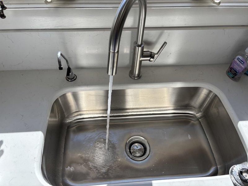 Installed customer-supplied garbage disposal unit with complete drain system reconfiguration, including installation of 2" x 1-1/2" x 1-1/2" sanitary tee, 2" coupling, and 1-1/2" no-hub band to accommodate new disposal configuration. Installed pull-down kitchen faucet with brushed stainless steel finish and reconnected reverse osmosis system with new 1/4" and 3/8" compression fittings, stiffeners, and ferrules. All fixtures tested and confirmed operational with no leaks detected.