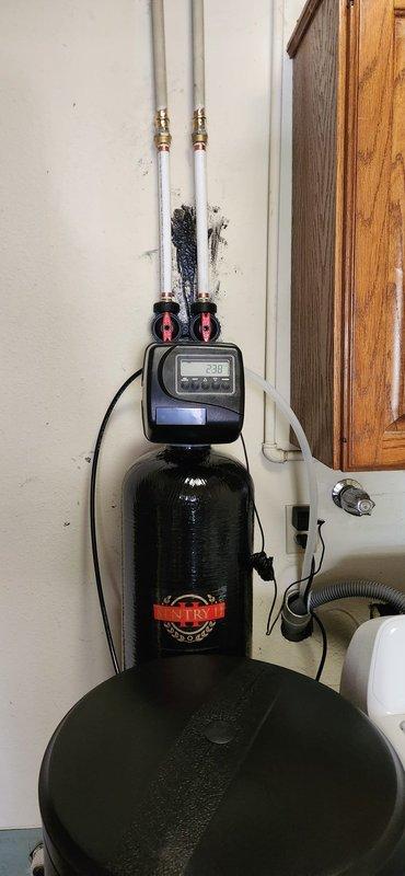 Installed 48,000 grain capacity water softener system with new brine tank in residential utility room. Connected unit to existing plumbing with white PEX supply lines and brass fittings, mounted black control valve with digital display, and filled brine tank with five bags of salt. Performed minor copper pipe repair during installation and programmed system settings to match house water hardness levels.