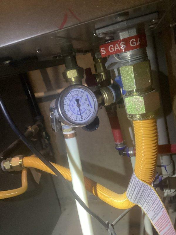 Responded to complaint of intermittent hot water from tankless water heater in basement, with unit cycling between hot and cold approximately every five minutes. Inspected 3.5-year-old tankless water heater system and associated gas supply components including pressure gauge, brass fittings, and CSST flexible gas lines. Documented gas connection assembly and system conditions through photographs for service records.