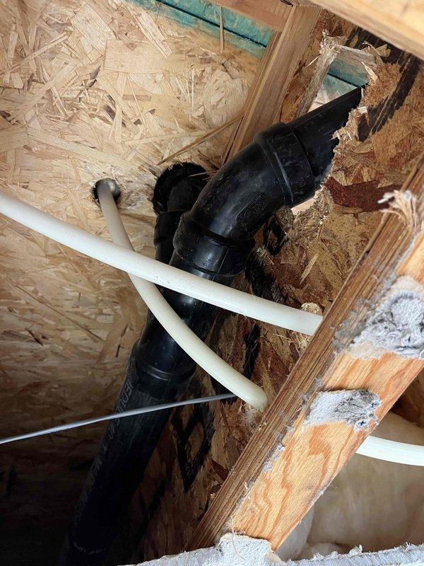 Responded to reported water leak originating from shower and penetrating to basement below. Upon inspection, accessed structural cavity between floors and identified compromised plumbing connections and deteriorated flexible drainage components. Documented existing conditions showing damaged black corrugated drain line with visible tears and deterioration, white PVC drainage pipes crossing through floor joists, and evidence of water intrusion in the structural space. Assessed mechanical systems, ductwork, and insulation in affected area to determine extent of leak damage and necessary repairs.