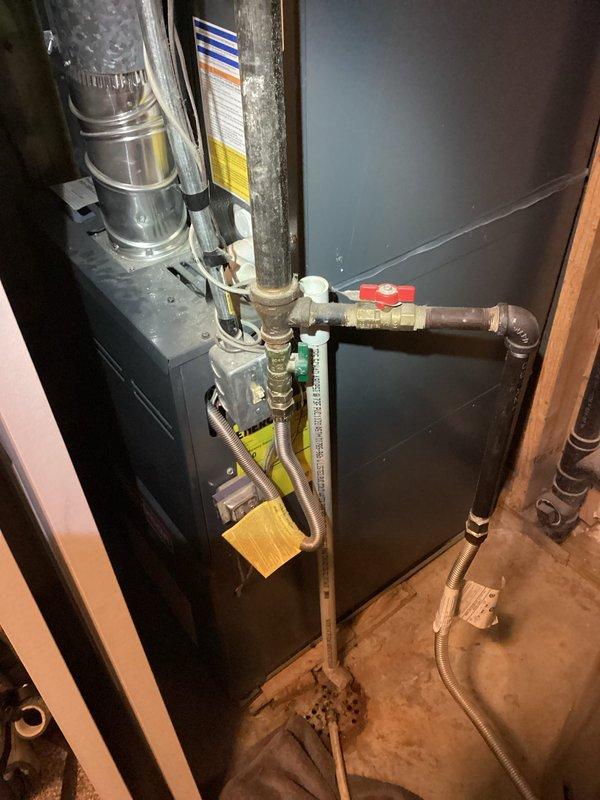 Responded to emergency call for furnace flooding in basement utility room. Upon arrival, found significant water accumulation in and around furnace unit, which was interfering with concurrent electrical work being performed. Inspected HVAC system including furnace, blower motor housing, and associated piping connections. Identified water intrusion issue affecting the heating system operation. Examined condensate drain system, evaporator coil area, and blower assembly to locate source of water discharge. Documented system condition with photos showing furnace installation, gas line connections with red and green valve handles, and interior view of cylindrical blower housing showing dust accumulation and wear patterns. Addressed immediate water issue to allow electrical repairs to proceed safely and prevent further damage to equipment and surrounding area.