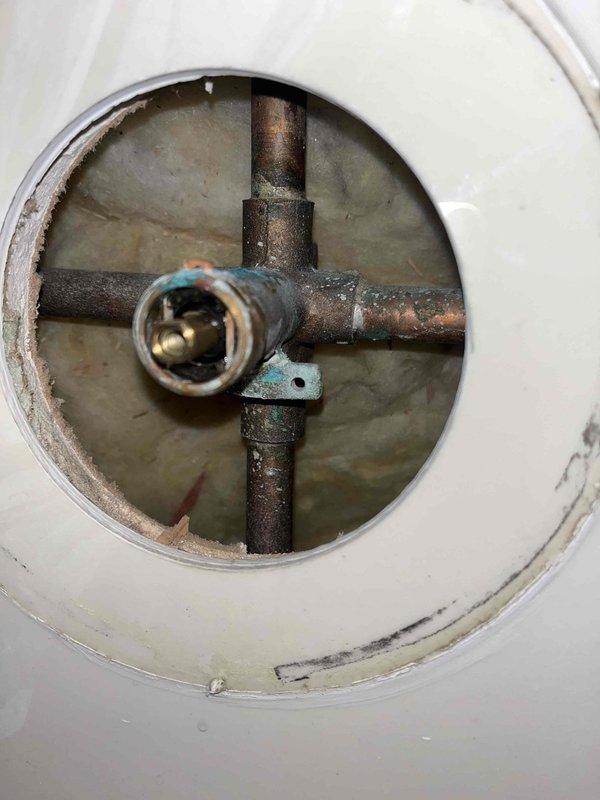 Responded to reported leak at bathroom sink with suspected shut-off valve failure and bathtub cartridge requiring replacement. Upon inspection, accessed main water shut-off valve assembly through floor access port and documented severely corroded cross-shaped pipe junction with significant rust, oxidation, and deterioration of metal components. Assessed central valve mechanism showing advanced age and corrosion, confirming need for shut-off valve replacement to address active leak and prevent further water damage.
