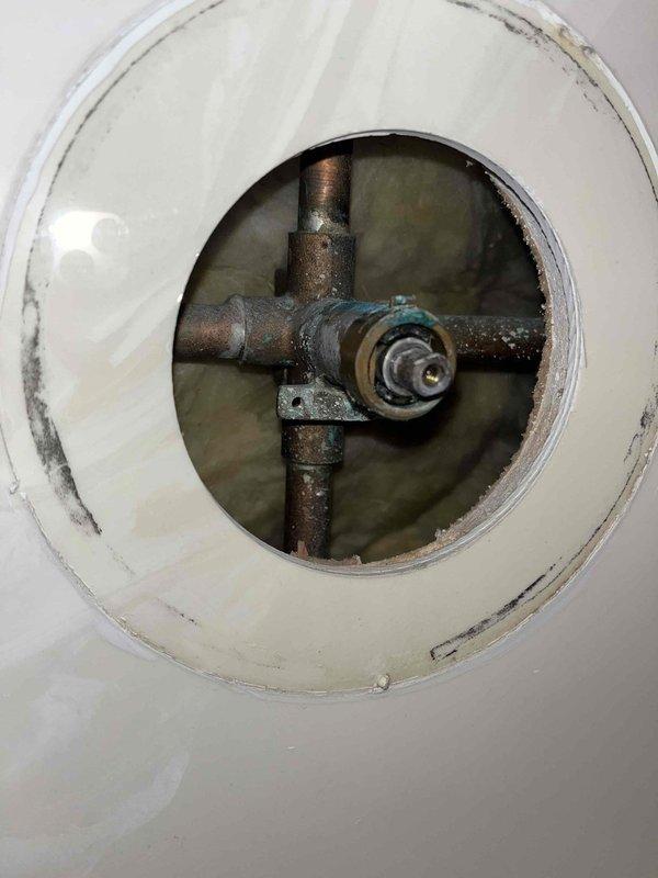Responded to reported leak at bathroom sink with suspected shut-off valve failure and bathtub cartridge requiring replacement. Upon inspection, accessed main water shut-off valve assembly through floor access port and documented severely corroded cross-shaped pipe junction with significant rust, oxidation, and deterioration of metal components. Assessed central valve mechanism showing advanced age and corrosion, confirming need for shut-off valve replacement to address active leak and prevent further water damage.