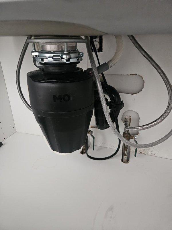 Responded to kitchen sink garbage disposal malfunction where unit was making noise when activated but not running. Upon inspection, diagnosed failed MOEN garbage disposal unit mounted beneath sink basin. Removed defective disposal unit from mounting assembly and installed replacement disposal, reconnecting drain lines and electrical power supply. Tested unit for proper operation and verified all connections were secure with no leaks.