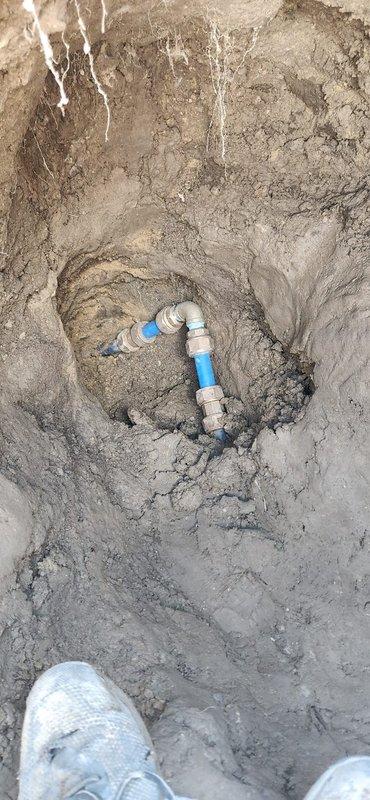 Completed warranty repair on main culinary water line outside residence. Excavated trench to expose compromised section of main water line, removed damaged pipe segment, and installed new blue PVC pipe with proper fittings and connections using beige coupling sections and gray threaded adapters. Backfilled excavation and restored site upon completion of spot repair.