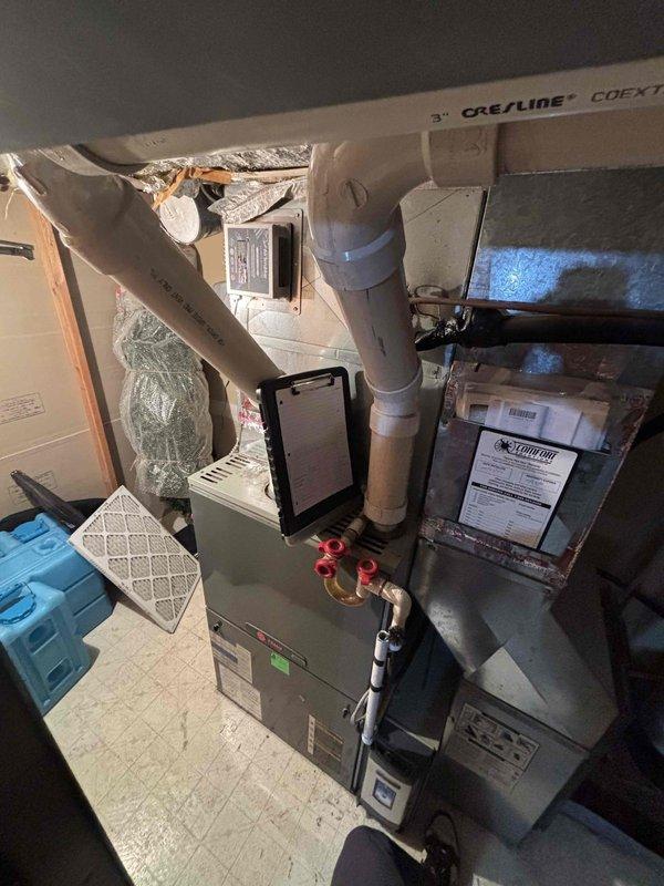 Responded to no-cooling call on residential split system with furnace located in garage. Upon arrival, confirmed outdoor unit not operating and no airflow from indoor unit. Diagnostic evaluation revealed fan motor failure causing system to enter high-pressure lockout condition. Further inspection identified restricted airflow due to impacted blower wheel and fouled evaporator coil contributing to system shutdown. System age assessed at 17 years for furnace and 21 years for air conditioning unit. Presented repair options and replacement recommendations based on equipment age and condition of major components including compressor, heat exchanger, and refrigerant lines. Photographed existing HVAC installation showing furnace with side-mounted filter, connected ductwork, refrigerant lines with service valves, and auxiliary equipment in mechanical space.