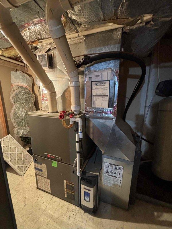 Responded to no-cooling call on residential split system with furnace located in garage. Upon arrival, confirmed outdoor unit not operating and no airflow from indoor unit. Diagnostic evaluation revealed fan motor failure causing system to enter high-pressure lockout condition. Further inspection identified restricted airflow due to impacted blower wheel and fouled evaporator coil contributing to system shutdown. System age assessed at 17 years for furnace and 21 years for air conditioning unit. Presented repair options and replacement recommendations based on equipment age and condition of major components including compressor, heat exchanger, and refrigerant lines. Photographed existing HVAC installation showing furnace with side-mounted filter, connected ductwork, refrigerant lines with service valves, and auxiliary equipment in mechanical space.