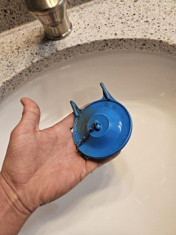 Responded to service call for toilet fill valve issue in bathroom. Upon inspection, found toilet tank with significant mineral buildup and discoloration indicating age-related wear. Assessed internal flushing mechanism including flush valve and fill valve assembly with float mechanism. Additionally inspected sink drain stopper assembly during visit. Diagnosed fill valve malfunction and completed necessary repairs to restore proper toilet function.