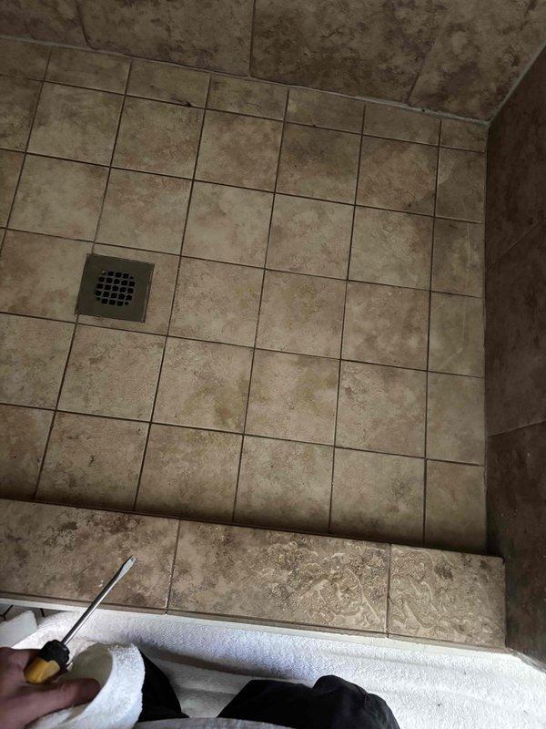 Replaced shower drain assembly and P-trap in tiled shower floor with oil-rubbed bronze finish drain cover. Accessed plumbing through ceiling below, requiring removal of drywall section to reach drain connection and trap. Ran mechanical auger through downstream piping to clear restrictions and improve drainage flow.