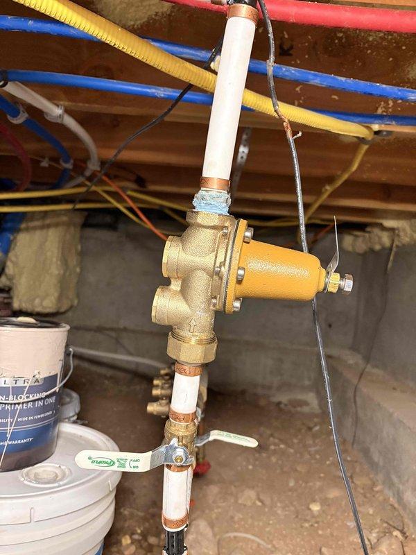 Responded to report of low water pressure affecting the property for approximately two weeks. Inspected existing brass pressure regulator valve assembly with PVC piping connections in basement utility area. Tested and measured water pressure using calibrated gauge to confirm pressure readings and verify regulator performance, determining that the pressure reducing valve required replacement to restore proper water pressure throughout the residence.