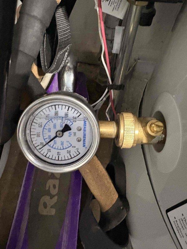 Responded to report of low water pressure affecting the property for approximately two weeks. Inspected existing brass pressure regulator valve assembly with PVC piping connections in basement utility area. Tested and measured water pressure using calibrated gauge to confirm pressure readings and verify regulator performance, determining that the pressure reducing valve required replacement to restore proper water pressure throughout the residence.
