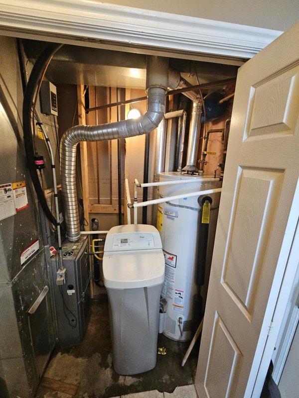 Responded to service call for leaking water heater in basement utility room. Upon inspection, identified active leak originating from top connections of 12+ year old tanked water heater with visible corrosion and rust present at base fittings and drain valve area. Provided customer with replacement options for consideration.