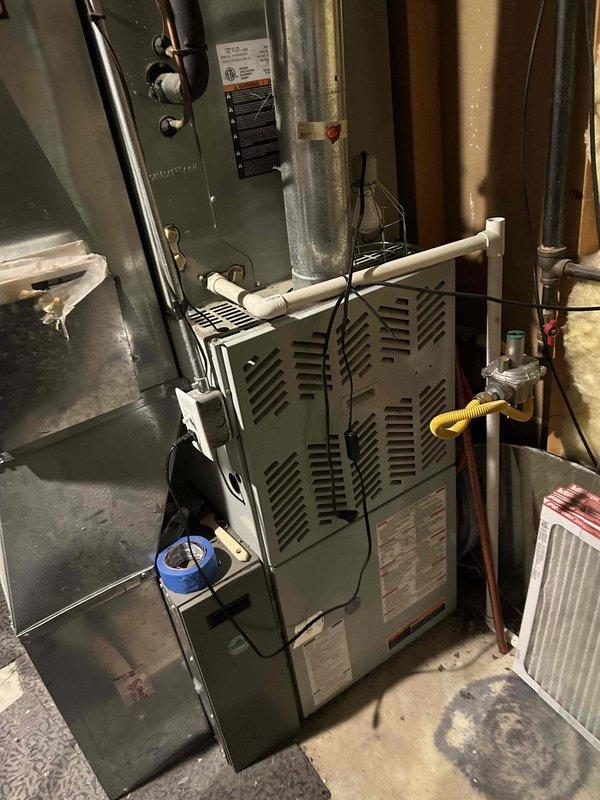 Completed membership maintenance inspection on residential HVAC system located in basement utility area. Performed comprehensive air conditioning tune-up including visual inspection of furnace unit, ductwork, and associated components. Verified gas line connections, shutoff valve operation, and proper installation of flexible gas connector. Inspected electrical connections, wiring, and control systems using Fieldpiece SC440 clamp meter to verify amperage readings and confirm system operating within normal parameters. Checked air filter condition and return air pathways for proper airflow. Documented equipment condition through photographic records showing furnace unit, plenum assembly, copper and PVC piping, and overall system configuration for maintenance history records.