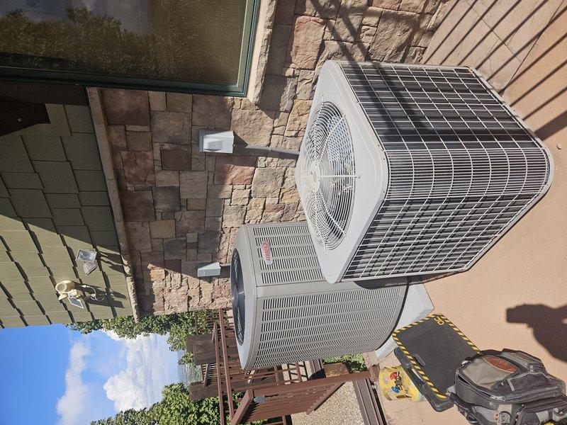 Temporarily relocated two 3-5 year old AC condenser units from driveway concrete pad to porch area to allow for concrete removal and driveway replacement. Disconnected electrical connections and refrigerant lines at terminal block, capped lines to prevent contamination, and safely moved both units to temporary location on wooden deck surface. Units secured and protected pending concrete completion for future reinstallation.