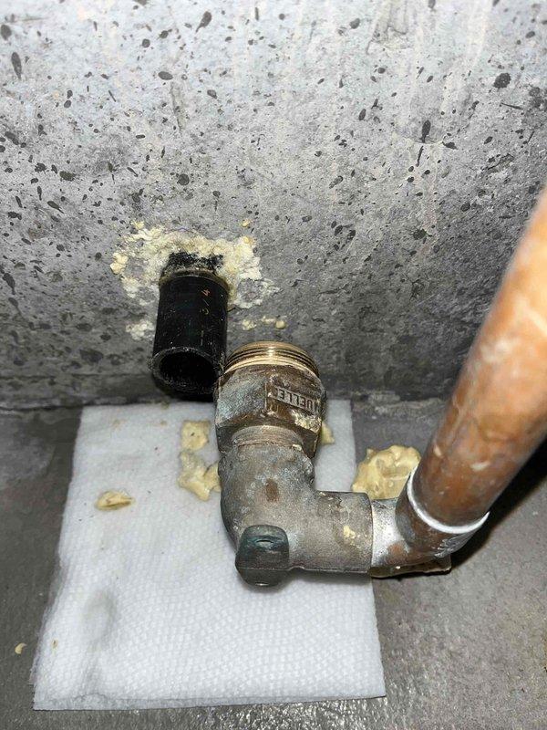 Responded to basement water pipe burst in aging plumbing system over 20 years old. Upon arrival, confirmed water supply had been shut off and standing water previously removed, with minor residual damage present. Inspected failed piping assembly consisting of corroded brass elbow fitting, deteriorated valve connection, and black pipe connector showing significant oxidation, mineral deposits, and weathering consistent with age and moisture exposure. Documented condition of compromised plumbing components mounted to concrete surface, noting extensive corrosion on metallic fittings and yellowish residue accumulation around connection points. Photographed failed assembly for assessment and records.