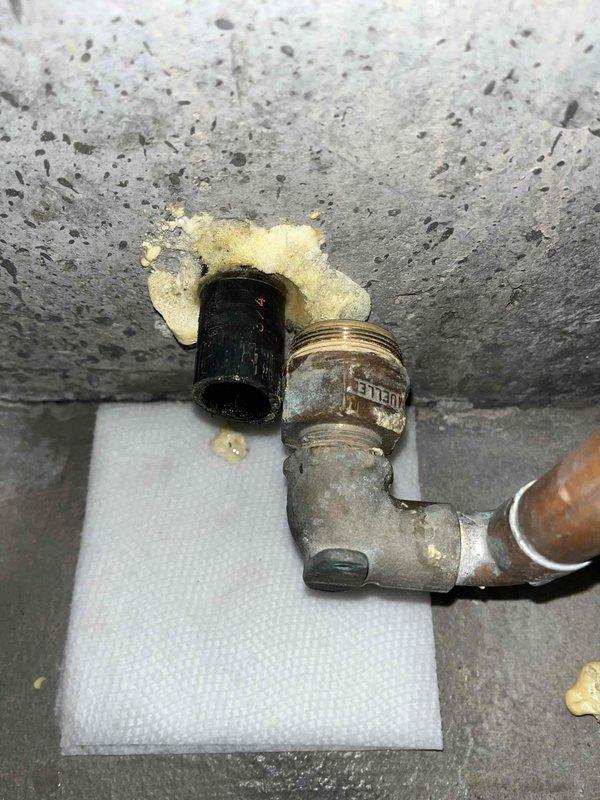 Responded to basement water pipe burst in aging plumbing system over 20 years old. Upon arrival, confirmed water supply had been shut off and standing water previously removed, with minor residual damage present. Inspected failed piping assembly consisting of corroded brass elbow fitting, deteriorated valve connection, and black pipe connector showing significant oxidation, mineral deposits, and weathering consistent with age and moisture exposure. Documented condition of compromised plumbing components mounted to concrete surface, noting extensive corrosion on metallic fittings and yellowish residue accumulation around connection points. Photographed failed assembly for assessment and records.