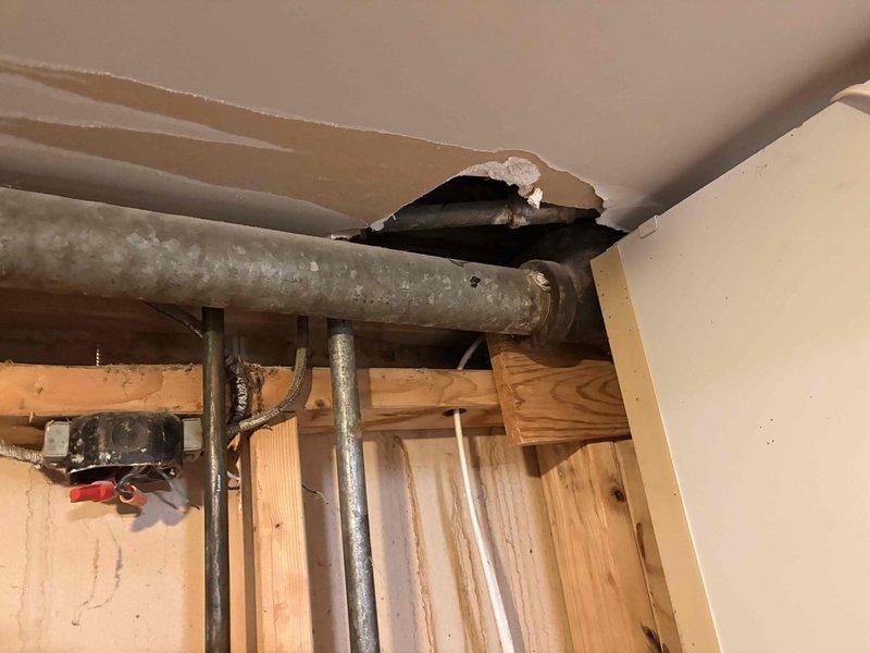 Responded to active sewer backup affecting multiple fixtures across two floors, including upstairs bathroom sink backing up into bathtub, downstairs shower backing up into laundry room drain, and gurgling kitchen sink. Accessed crawlspace and inspected main drain line system, identifying blockage in primary waste line causing cross-fixture backup conditions. Documented exposed plumbing infrastructure showing frost accumulation on horizontal drain pipes and compromised ceiling access points where main stack and branch lines converge at structural framing.