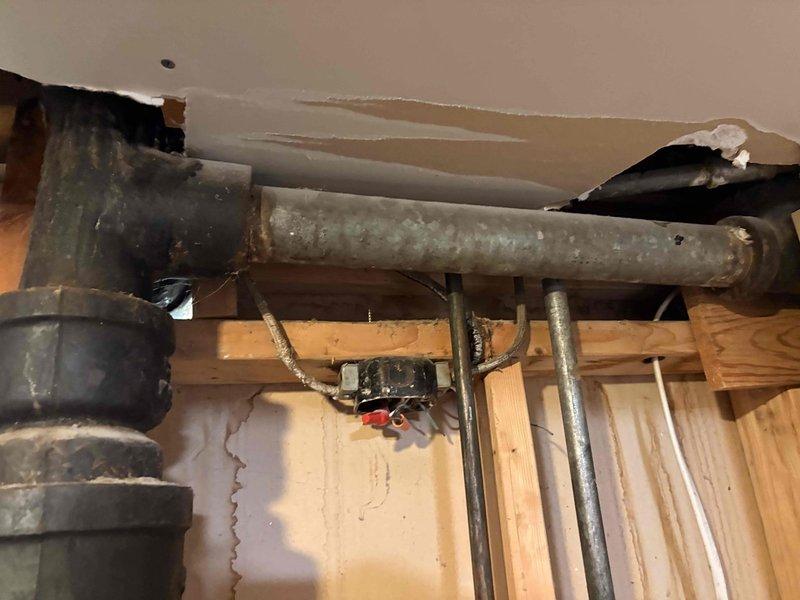 Responded to active sewer backup affecting multiple fixtures across two floors, including upstairs bathroom sink backing up into bathtub, downstairs shower backing up into laundry room drain, and gurgling kitchen sink. Accessed crawlspace and inspected main drain line system, identifying blockage in primary waste line causing cross-fixture backup conditions. Documented exposed plumbing infrastructure showing frost accumulation on horizontal drain pipes and compromised ceiling access points where main stack and branch lines converge at structural framing.