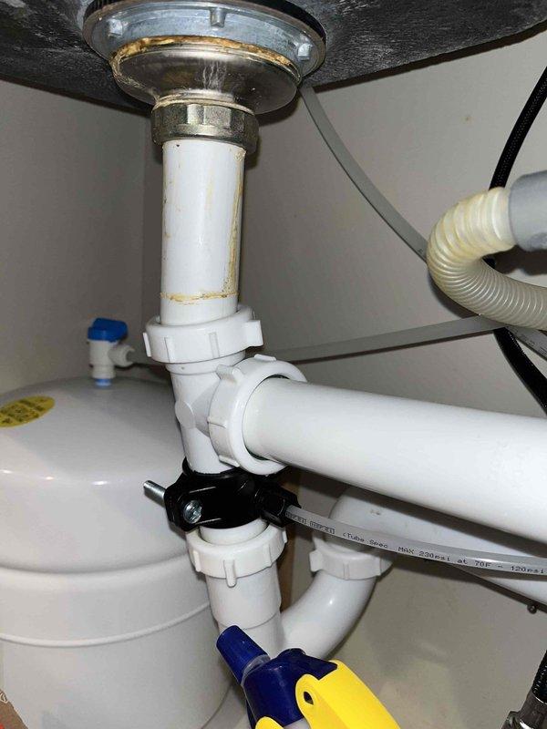 Completed annual plumbing maintenance visit under membership plan, including comprehensive system pressure test, water purity analysis, and water heater flush. Inspected under-sink plumbing assembly, noting discoloration on vertical drain pipe below metal strainer and examining PVC P-trap connections with visible wear on chrome fixtures. Documented pipe cross-section showing insulation layers and conductor core, along with overall drain assembly condition including blue valve connection and corrugated supply line.
