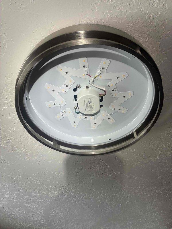 Responded to service call for assistance with ceiling-mounted LED light fixture in main level living room that customer had removed for cleaning and was unable to reinstall. Upon arrival, assessed the fixture components including the LED array circuit board, driver/transformer with associated wiring, and ceiling mounting hardware. Successfully reconnected electrical wiring, secured the driver unit to the junction box, properly seated the LED array and trim ring assembly, and restored the fixture to full operation with secure ceiling mounting.