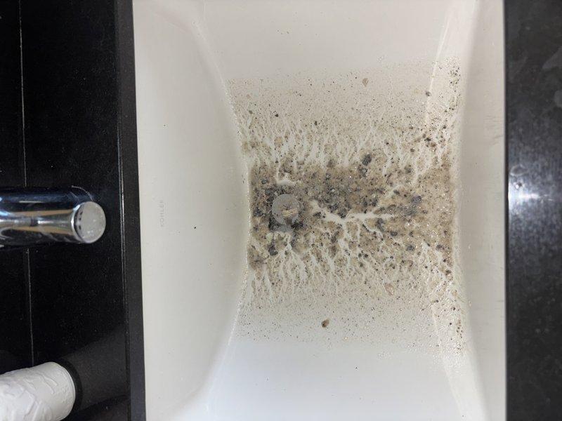 Completed comprehensive plumbing membership inspection of residential water supply system and fixtures. Documented condition of bathroom sink showing accumulation of sediment and mineral deposits around drain area requiring routine cleaning maintenance. Inspected mechanical room plumbing infrastructure including water heater connections, multiple supply lines with braided stainless steel flex hoses, brass fittings, shut-off valves, and what appears to be water filtration or expansion tank equipment, confirming all connections are secure and system components are properly installed.