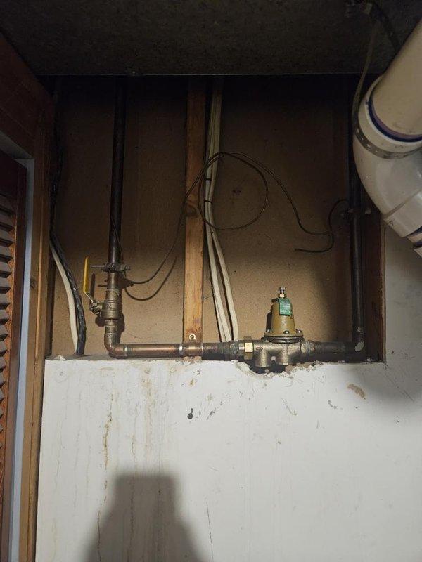 Responded to service call for moisture accumulation at base of 16-year-old residential tank-style water heater located in basement. Upon inspection, identified significant corrosion and oxidation on copper supply piping and brass valve assembly, with visible green patina indicating extended exposure to moisture. Observed deteriorated plumbing connections with evidence of slow leaking at tank base and pressure relief valve discharge piping. Water heater showed advanced age-related degradation with corroded fittings and compromised integrity of tank bottom. Documented condition of existing plumbing infrastructure including pressure regulator valves, supply lines, and mounting hardware. Assessed water damage to surrounding wall surfaces and floor area beneath unit. Provided comprehensive evaluation of water heater system and recommended full tank replacement due to age of equipment exceeding typical service life and active leak condition presenting risk of catastrophic failure.