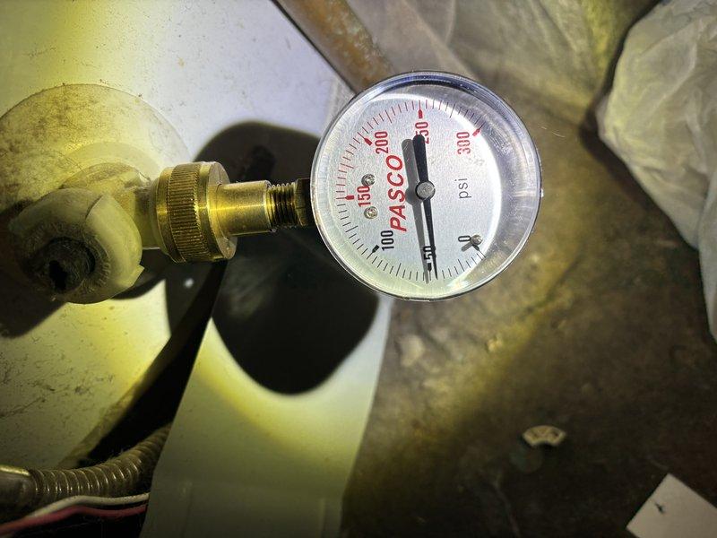 Inspected the upstairs tub drain assembly from below and found the ABS drain and tailpiece connection at the tub outlet to be the source of the leak, with water staining and organic growth on the surrounding framing and subfloor from prolonged moisture exposure. Evaluated the drain connections and trap arm coupling for leakage and verified system water pressure at the nearby water heater using a pressure gauge (approximately 50 psi) to rule out excessive pressure as a contributing factor.