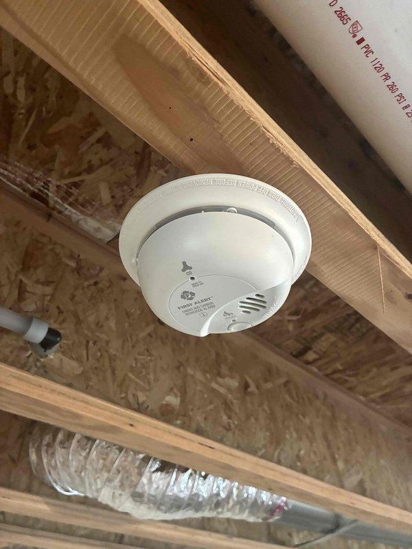 Performed an electrical maintenance inspection of the main service panel with the cover removed, visually checking the breakers, conductors, main lugs, and circuit labeling. Observed organized branch circuit wiring with labeled conductors and noted wood shavings debris at the bottom of the panel enclosure. Verified the combination smoke/carbon monoxide alarm mounted to the framing was in place and free of visible damage, corrosion, or defects, with no other deficiencies identified.