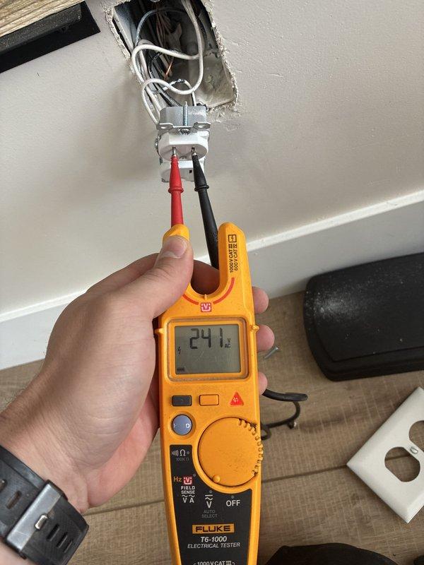 Troubleshot a non-functioning front doorbell and verified 241 V AC at the receptacle terminals with a clamp meter and tester, confirming line voltage was present at the box and the fault was not a loss of supply. Removed the cover plate and inspected the wiring in the recessed metal box to evaluate the doorbell transformer circuit.