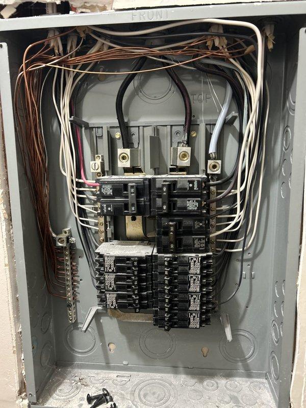 Performed preventative electrical maintenance inspection of the main service panel with the cover removed, evaluating service conductor terminations at the main lugs, neutral/ground bus bar connections, and breaker condition. Observed densely packed, loosely routed conductors and chipped plaster/drywall damage around the enclosure, with debris and loose screws in the bottom of the panel. Also inspected a kitchen GFCI receptacle and noted heavy crumb and burnt debris buildup in the adjacent toaster slots, a potential fire and shock hazard recommended for cleaning.
