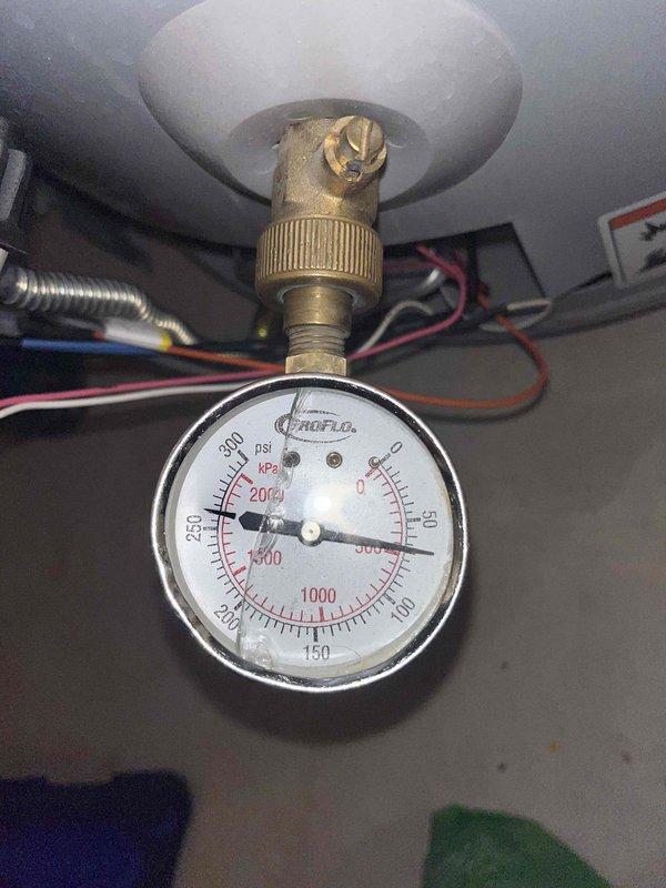 Diagnosed a 7-year-old A.O. Smith 50-gallon tanked water heater producing only lukewarm water; the status light flashed a six-blink fault code that indicates burner assembly replacement. During inspection, found a cracked-lens ProFlo pressure gauge threaded onto a brass fitting at the base of the tank, reading approximately 100 psi, and noted a worn, chipped valve stem on the fitting. Documented the findings and presented repair options, including burner assembly replacement, to restore full hot water output.