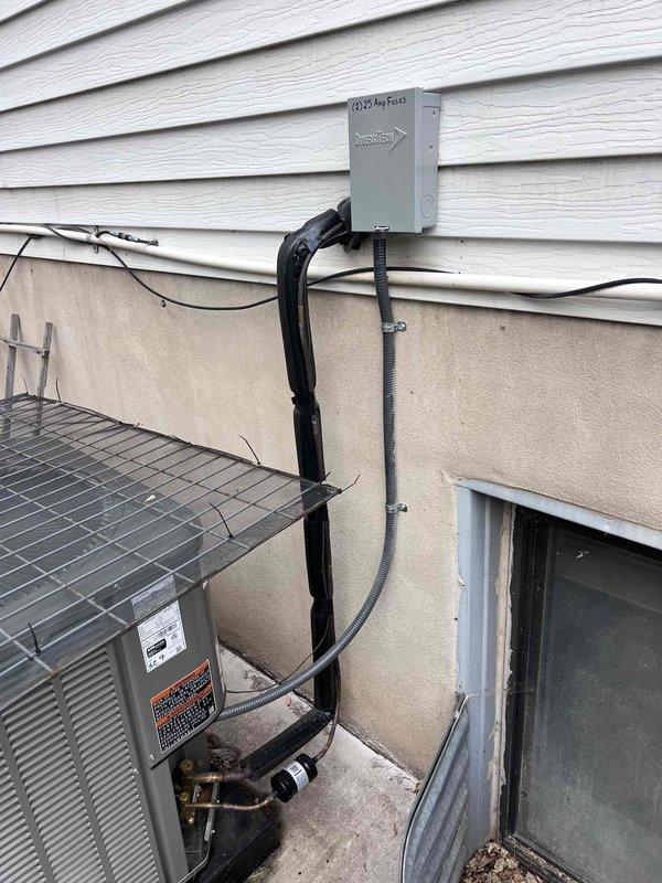 Performed warranty recall to correct failed inspection items on the AC installation. Secured the condensate drain line and flexible hose at the floor drain with a zip tie and clamp so the line remains properly terminated at the drain, and verified the flexible conduit (AC whip) is secured to the disconnect within the 8-inch maximum. Confirmed the condenser, refrigerant lines, and electrical connections are in good condition with no visible damage, and documented the corrected work with photos.