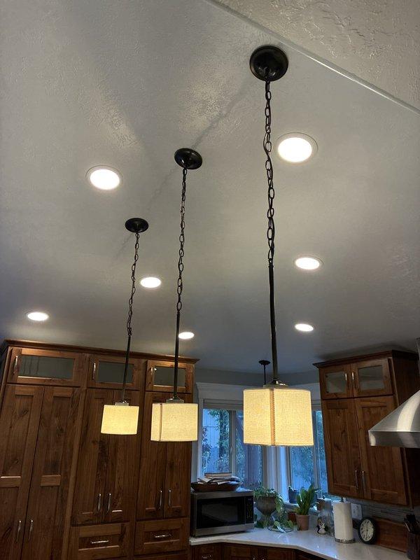Removed existing light fixtures over the kitchen island and dining table and installed three new pendant lights with dark bronze canopies and fabric shades above the island, along with a new chandelier over the kitchen table. Made all electrical connections, secured the fixtures to the ceiling boxes at staggered pendant heights, and tested for proper operation. The new fixtures function correctly, and the existing recessed LED lighting was left undisturbed.